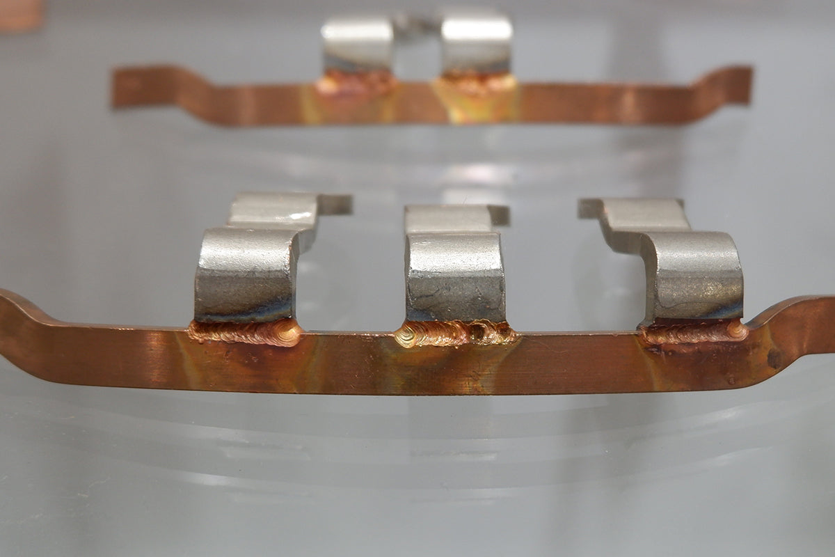 Copper and steel connector pieces joined with precision laser welding, showing smooth and consistent weld seams.