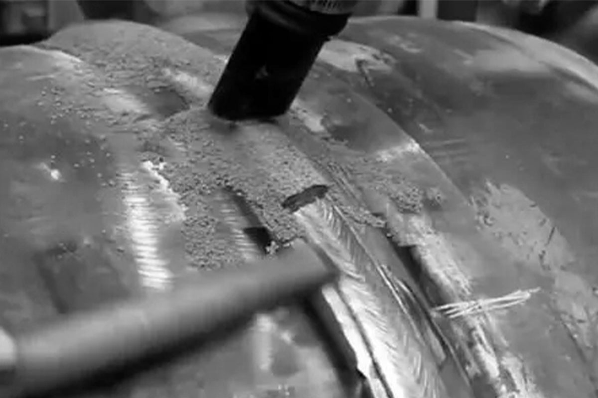 Worker grinding traditional welded metal surface with visible heat distortion and rough weld seams.