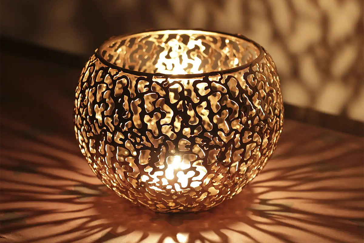 Laser-welded metal candle holder with intricate perforated patterns.