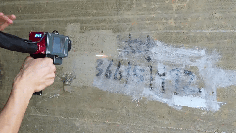 Laser cleaning machine removing graffiti from wall surface using non-contact fiber laser technology.