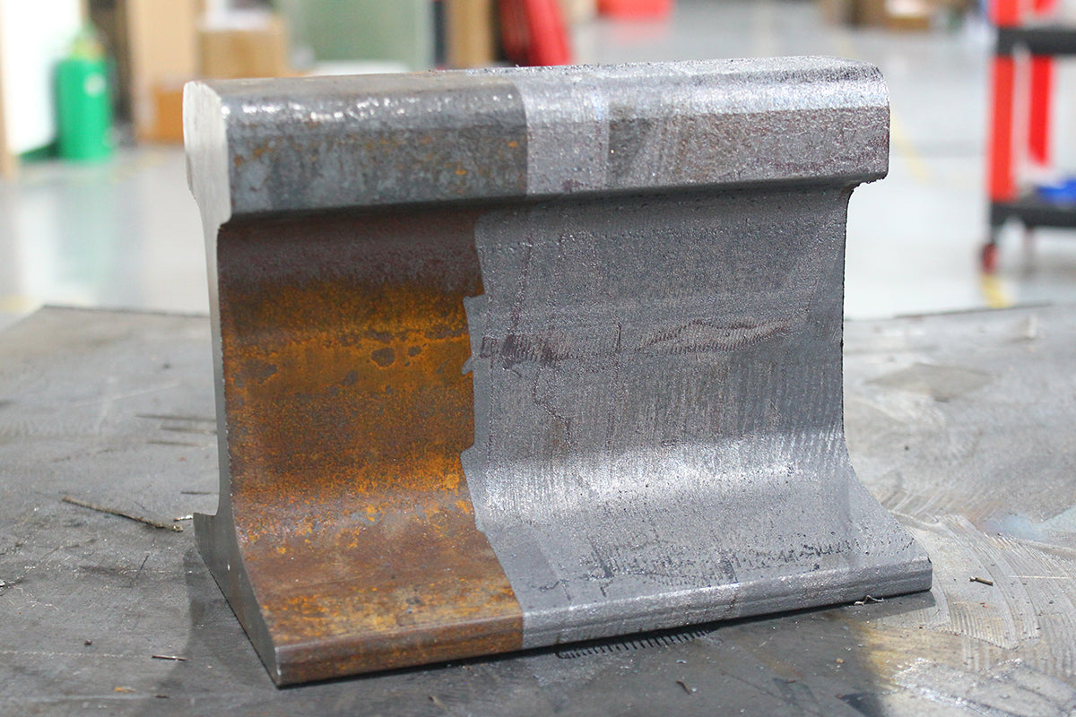 Steel rail track section showing rust and cleaned surfaces for before-and-after laser rust removal comparison.